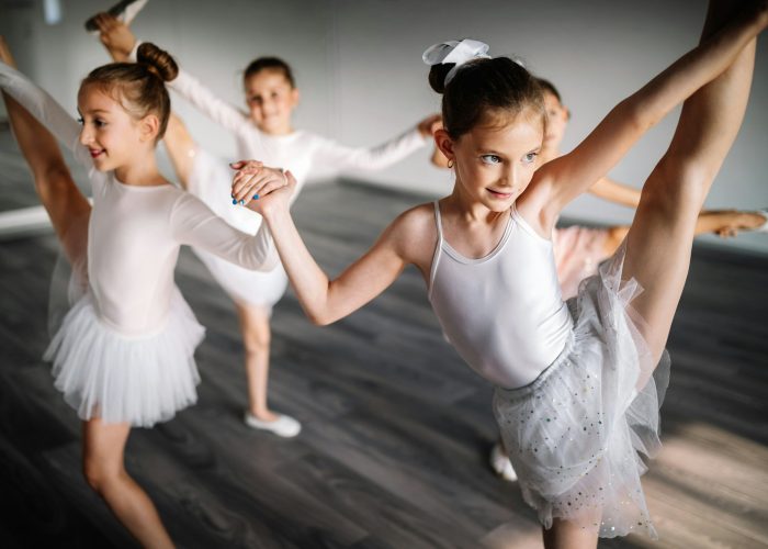 Group of fit happy children exercising ballet in studio together